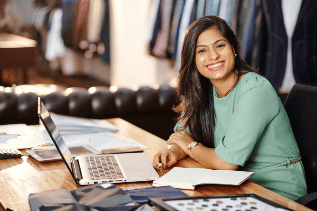 young, smiling female entrepreneur sitting at her work desk, with a laptop